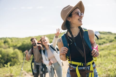 Three cheerful friends enjoying sunny day while walking and hiking in countryside