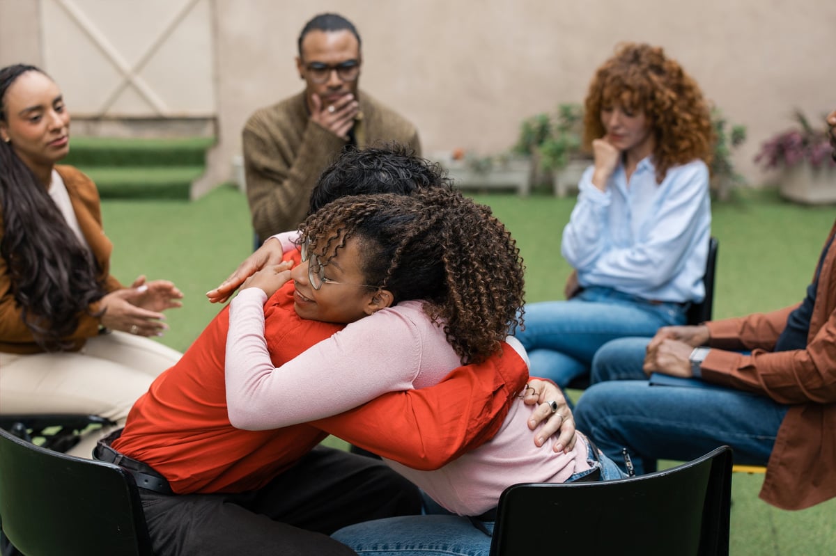 People showing empathy and support by hugging during a mental health group therapy session, fostering wellness and emotional healing